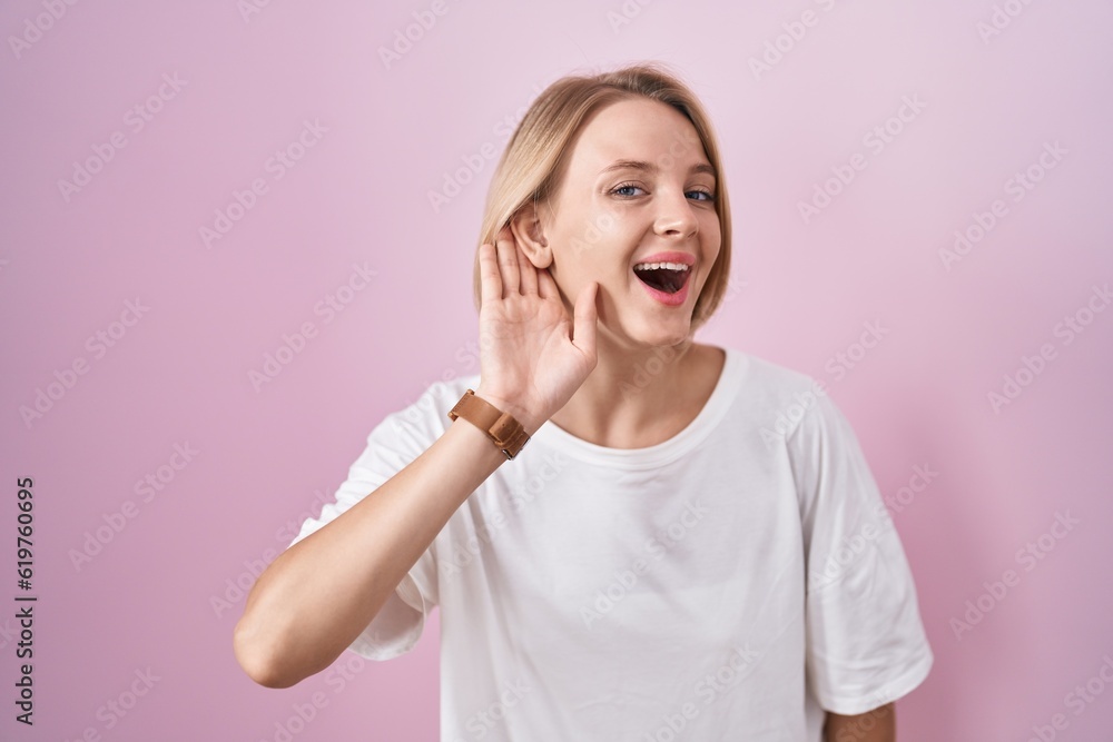 Young caucasian woman standing over pink background smiling with hand over ear listening an hearing to rumor or gossip. deafness concept. Young caucasian woman standing over pink background smiling with hand over ear listening an hearing to rumor or gossip. deafness concept.
