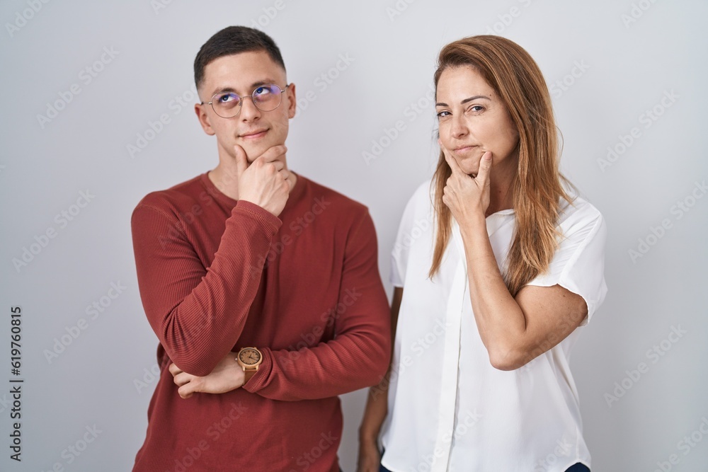 Mother and son standing together over isolated background looking confident at the camera smiling with crossed arms and hand raised on chin. thinking positive. Mother and son standing together over isolated background looking confident at the camera smiling with crossed arms and hand raised on chin. thinking positive.