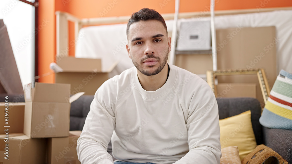 Young hispanic man sitting on sofa with serious expression at new home Young hispanic man sitting on sofa with serious expression at new home