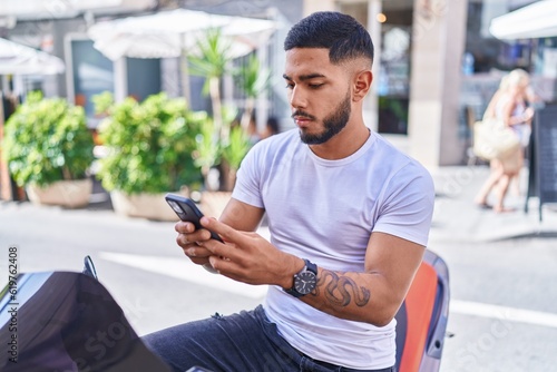 Young latin man using smartphone sitting on motorbike at street