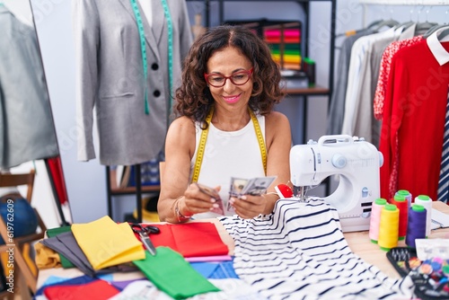 Middle age woman tailor smiling confident counting dollars at clothing factory