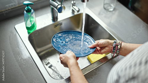 Middle age hispanic woman washing plates at the kitchen
