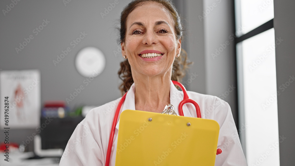 Middle age hispanic woman doctor smiling confident holding clipboard at clinic Middle age hispanic woman doctor smiling confident holding clipboard at clinic