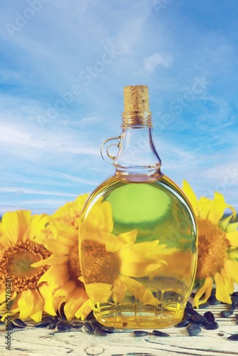 A bottle of sunflower oil  fresh sunflower flowers and seeds on the table  on the background of a landscape with a blooming field  summer  autumn