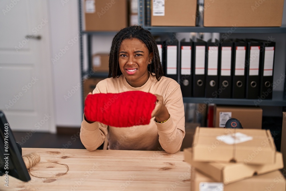 Young african american with braids working at textile business ecommerce clueless and confused expression. doubt concept.