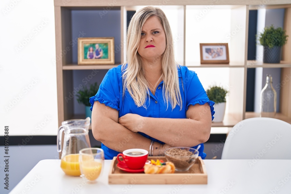 Caucasian plus size woman eating breakfast at home skeptic and nervous, disapproving expression on face with crossed arms. negative person.