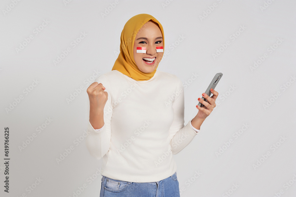 Excited young Asian Muslim woman wearing a hijab using smartphone and ...