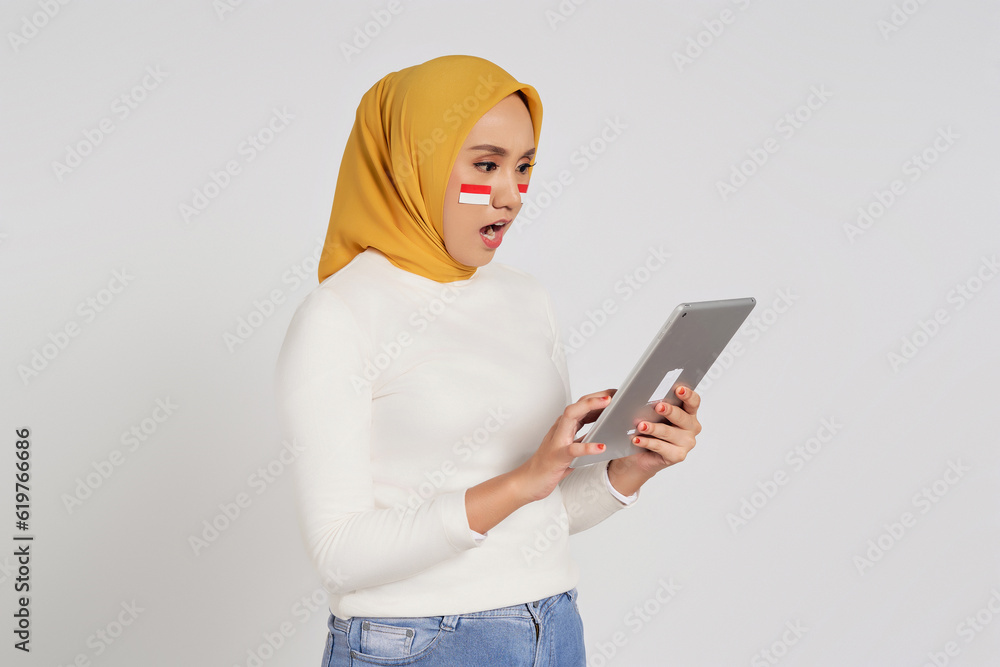 Surprised young Asian Muslim woman wearing a hijab using digital tablet isolated over white background. Celebrate Indonesian independence day on 17 August Surprised young Asian Muslim woman wearing a hijab using digital tablet isolated over white background. Celebrate Indonesian independence day on 17 August