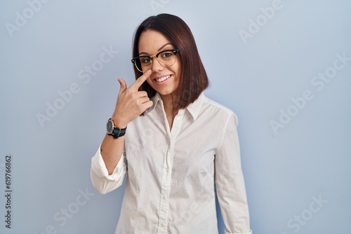 Young hispanic woman standing over white background pointing with hand finger to face and nose, smiling cheerful. beauty concept