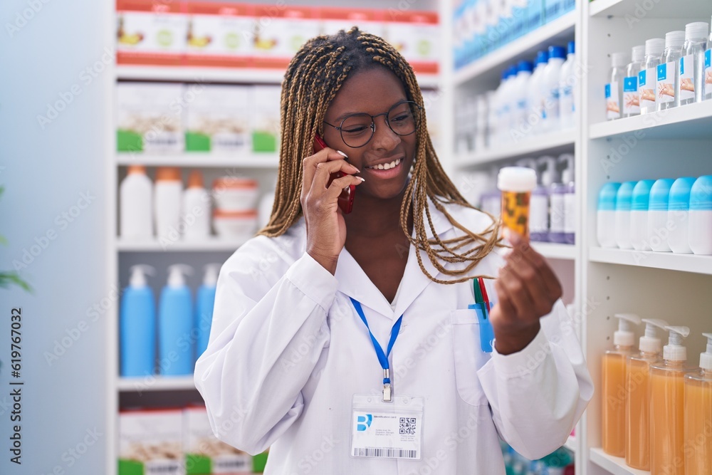 African american woman pharmacist holding pills bottle talking on smartphone at pharmacy