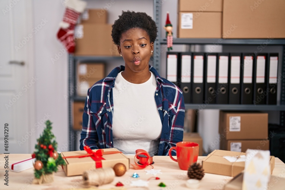 Fototapeta premium African american woman working at small business doing christmas decoration making fish face with lips, crazy and comical gesture. funny expression.