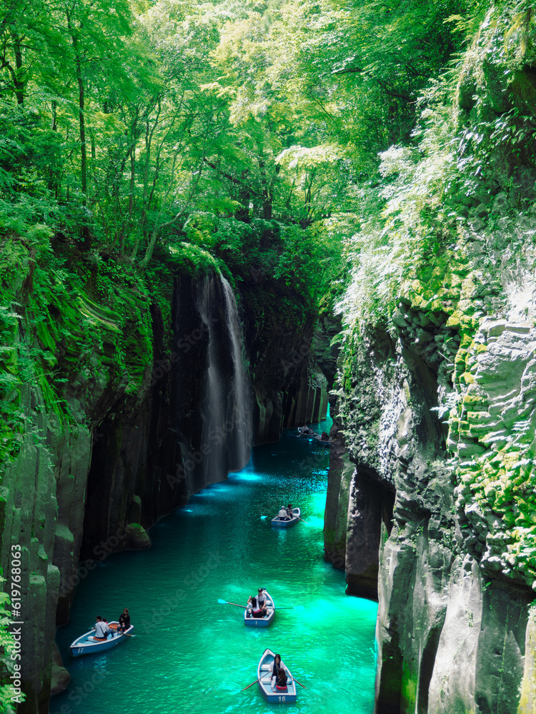 Naklejka premium Under fresh greenery, people enjoy boating at Takachiho Gorge, a famous tourist attraction in Miyazaki Prefecture, Japan