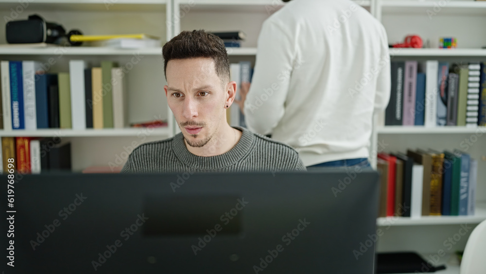 Two men students using computer studying at library university Two men students using computer studying at library university
