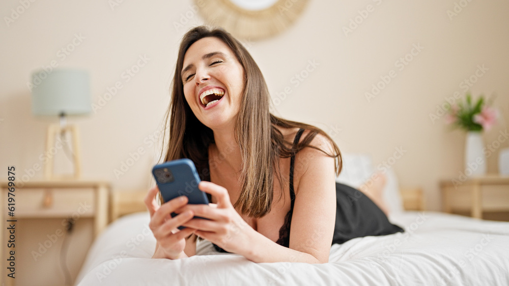 Young beautiful hispanic woman using smartphone lying on bed at bedroom Young beautiful hispanic woman using smartphone lying on bed at bedroom