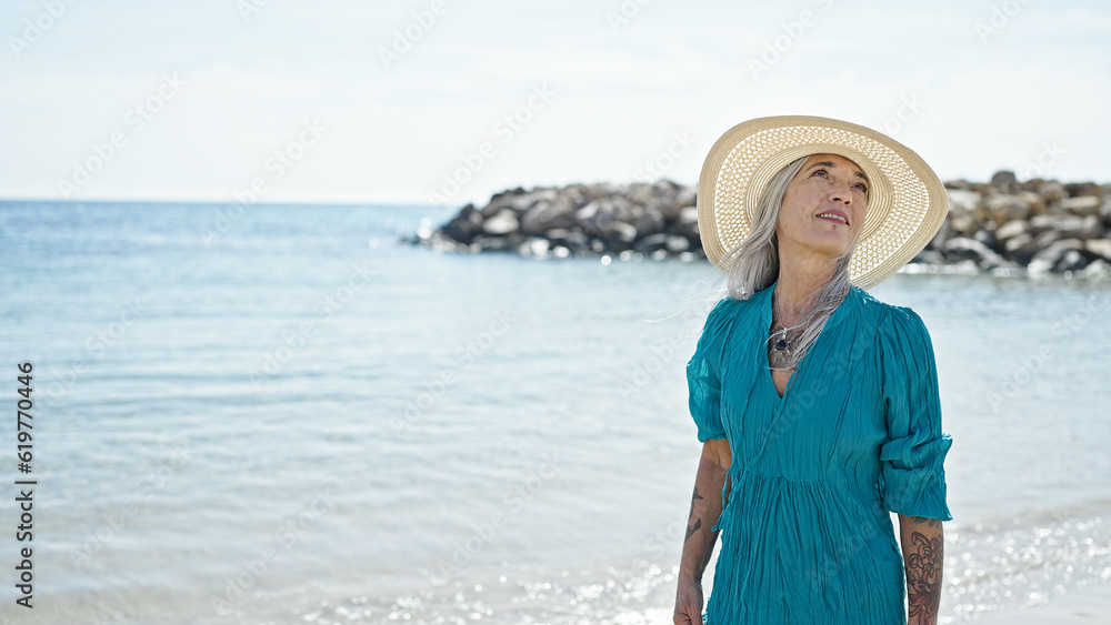 Middle age grey-haired woman tourist smiling confident walking at beach