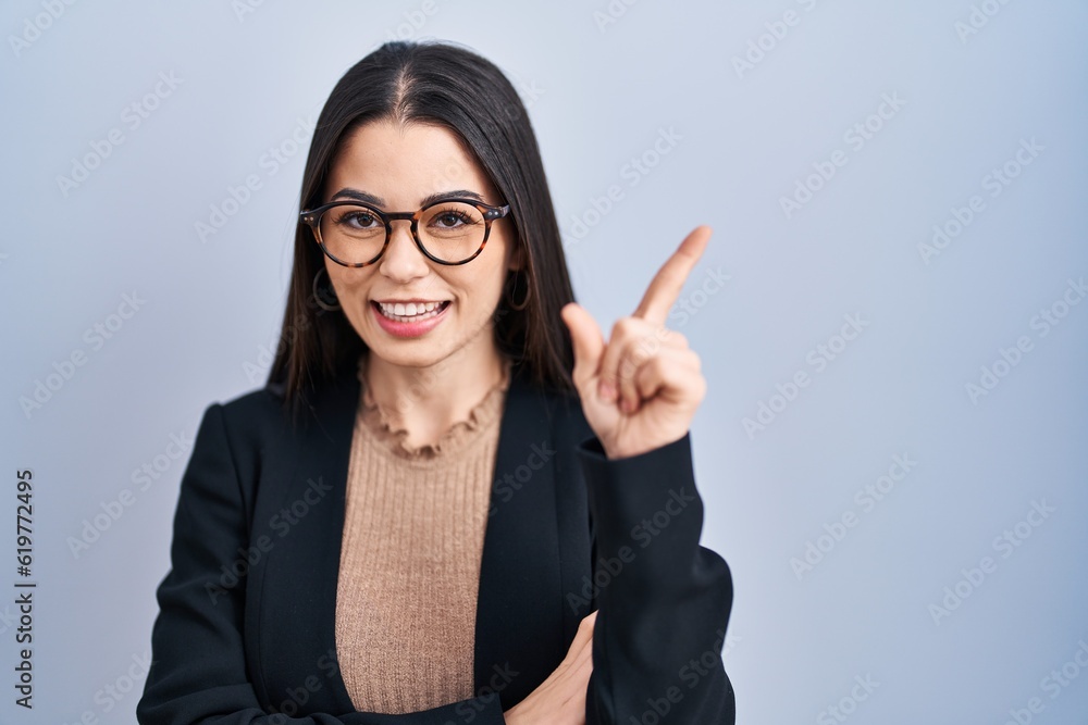 Young brunette woman standing over blue background with a big smile on face, pointing with hand and finger to the side looking at the camera. Young brunette woman standing over blue background with a big smile on face, pointing with hand and finger to the side looking at the camera.