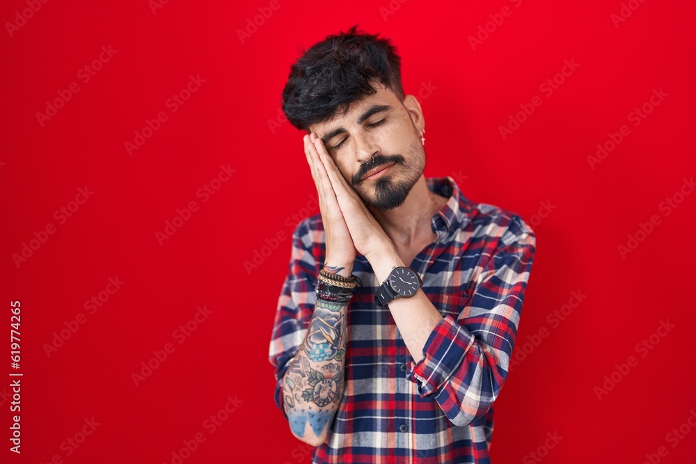 Young hispanic man with beard standing over red background sleeping tired dreaming and posing with hands together while smiling with closed eyes. Young hispanic man with beard standing over red background sleeping tired dreaming and posing with hands together while smiling with closed eyes.