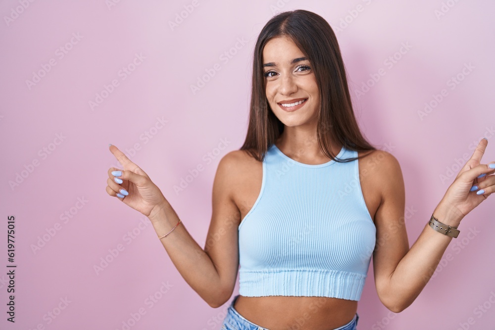 Young brunette woman standing over pink background smiling confident pointing with fingers to different directions. copy space for advertisement