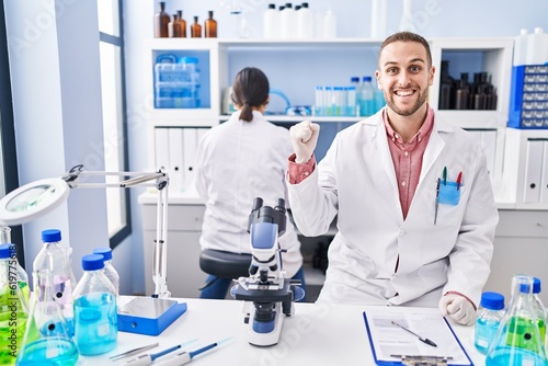 Young man working at scientist laboratory screaming proud  celebrating victory and success very excited with raised arm