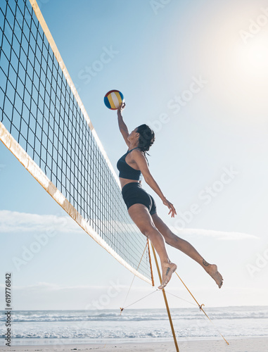 Woman, jump and volleyball in air on beach by net in serious sports match, game or competition. Fit, active and sporty female person jumping or reaching for ball in volley or spike by the ocean coast