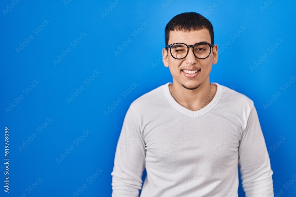 Young arab man wearing casual white shirt and glasses winking looking at the camera with sexy expression, cheerful and happy face. Young arab man wearing casual white shirt and glasses winking looking at the camera with sexy expression, cheerful and happy face.
