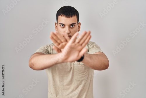 Young arab man wearing casual t shirt rejection expression crossing arms and palms doing negative sign, angry face