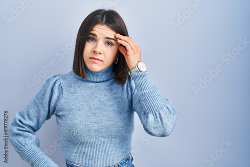 Young hispanic woman standing over blue background worried and stressed about a problem with hand on forehead, nervous and anxious for crisis