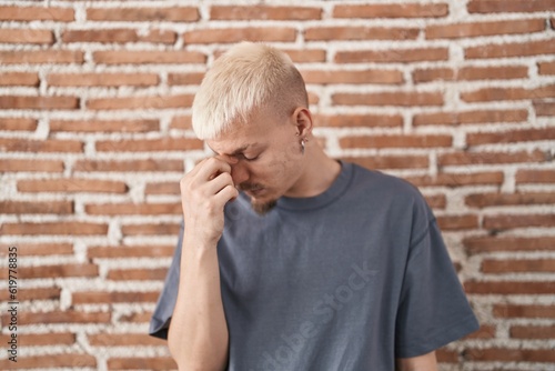 Young caucasian man standing over bricks wall tired rubbing nose and eyes feeling fatigue and headache. stress and frustration concept. © Krakenimages.com