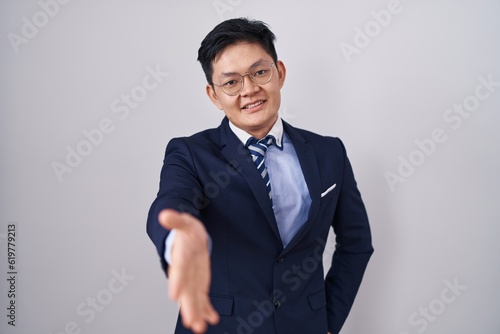 Young asian man wearing business suit and tie smiling friendly offering handshake as greeting and welcoming. successful business.