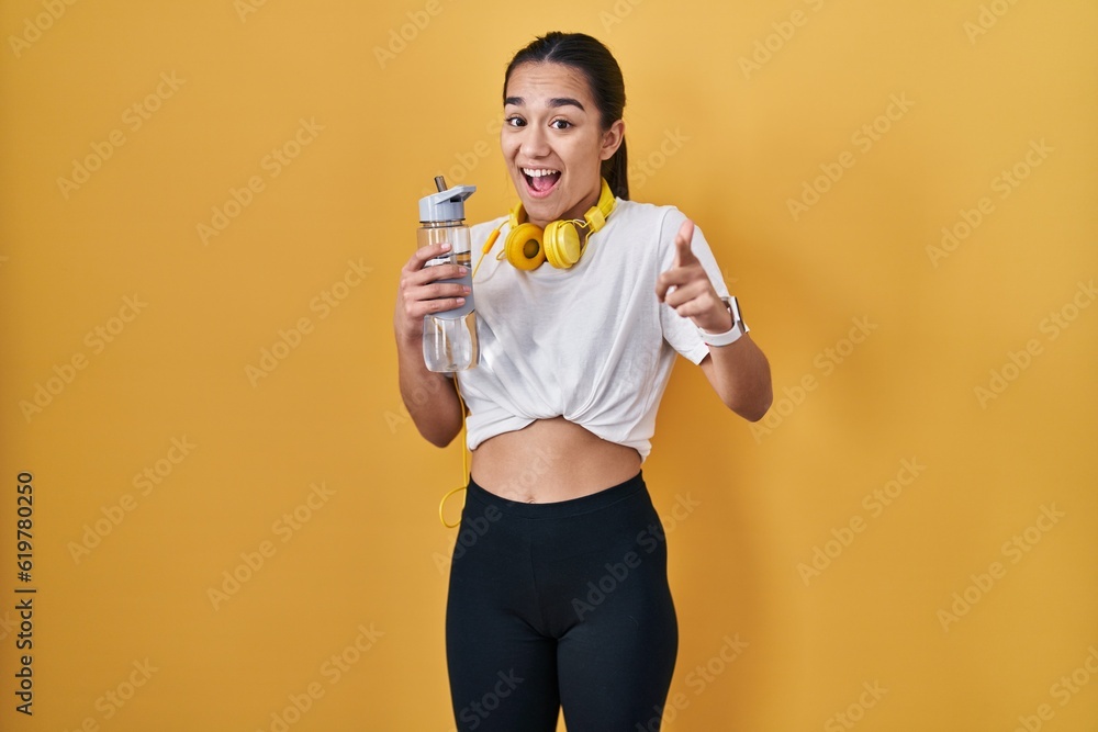 Young south asian woman wearing sportswear drinking water pointing fingers to camera with happy and funny face. good energy and vibes. Young south asian woman wearing sportswear drinking water pointing fingers to camera with happy and funny face. good energy and vibes.