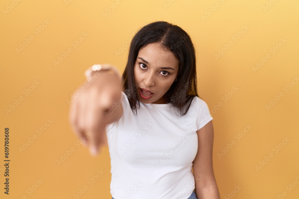 Young arab woman wearing casual white t shirt over yellow background pointing displeased and frustrated to the camera, angry and furious with you Young arab woman wearing casual white t shirt over yellow background pointing displeased and frustrated to the camera, angry and furious with you
