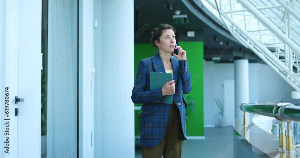 business woman standing in the business centre and talking on the phone with laptop. High quality video footage business woman standing in the business centre and talking on the phone with laptop. High quality video footage