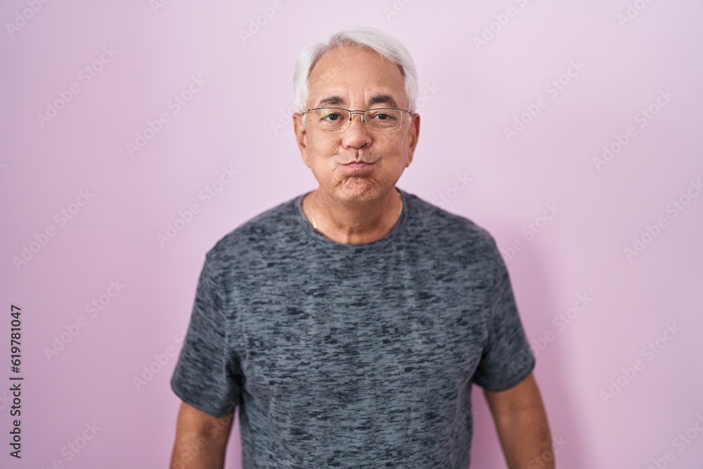 Middle age man with grey hair standing over pink background puffing cheeks with funny face. mouth inflated with air, crazy expression. Middle age man with grey hair standing over pink background puffing cheeks with funny face. mouth inflated with air, crazy expression.