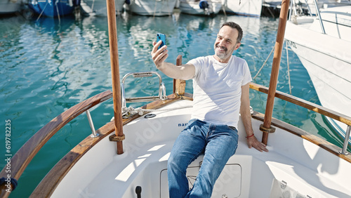 Middle age man make selfie by smartphone sitting on boat at port