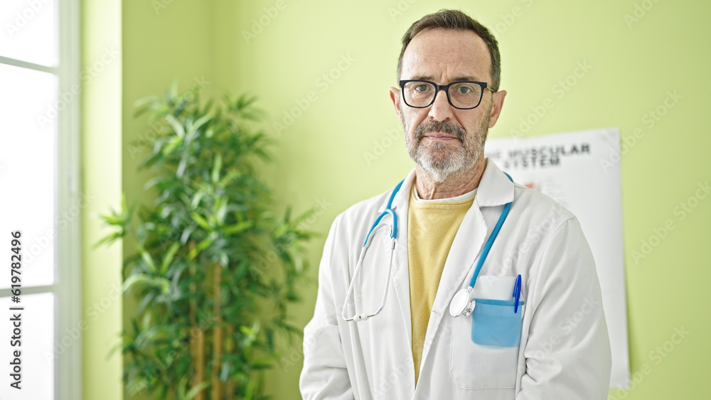 Middle age man doctor standing with serious expression at clinic Middle age man doctor standing with serious expression at clinic
