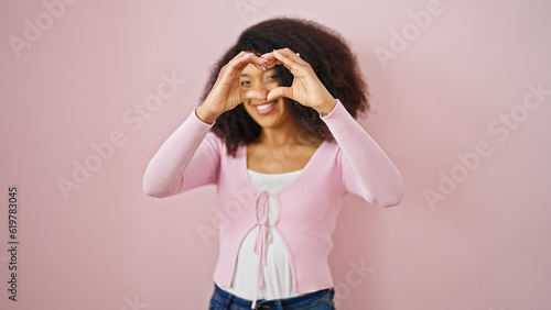 African american woman smiling confident doing heart gesture with hands over isolated pink background