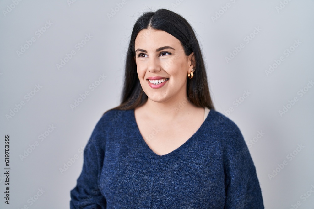 Young brunette woman standing over isolated background looking away to side with smile on face, natural expression. laughing confident.