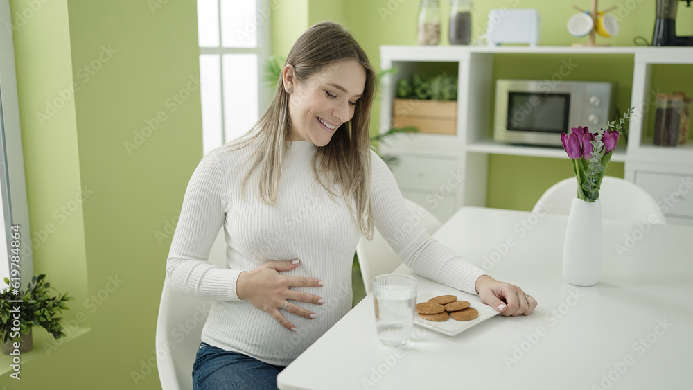 Young pregnant woman eating cookies sitting on table at dinning room Young pregnant woman eating cookies sitting on table at dinning room