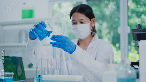 Female scientist or researcher is pouring blue substance or liquid in to a sample test tube. Concept of science, biochemistry, chemical, biotechnology laboratory. Substance study analyzing experiment