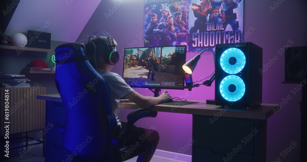 Young gamer plays third person shooter on personal computer. Schoolboy
