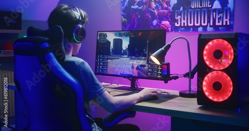 Fotografie Young gamer in headphones plays in first person shooter on computer