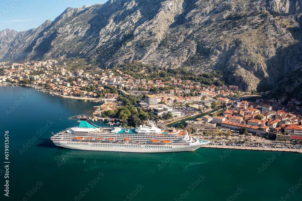Obraz premium Aerial panoramic view of the picturesque town of Kotor with beautiful coastline, promenade, red roofs, marina with boats and big cruise ship, Montenegro