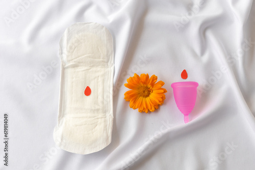 Reusable menstrual cup, calendula and  sanitary napkins on white cloth, concept female intimate hygiene period products and zero waste. Minimalism. Top view.  photo