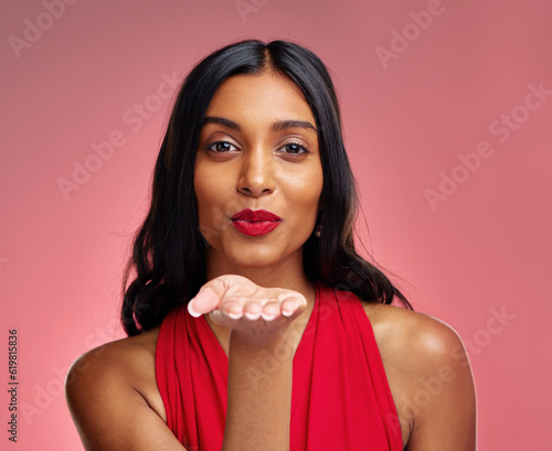 Woman, red lipstick and beauty, blow kiss with makeup and flirt, cosmetics and glow on pink background. Cosmetology, Indian female model pout with color in portrait and shine with wellness in studio