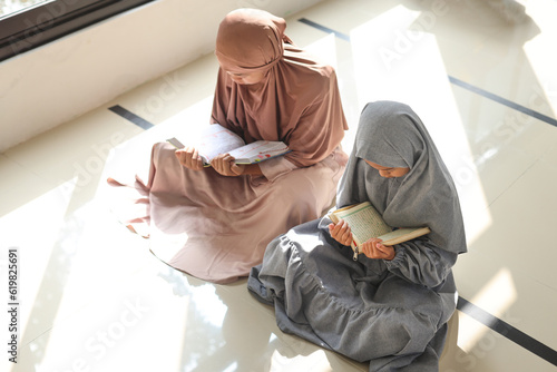Photography Two little Muslim girls reading Quran Holy Book near window of the mosque, top v
