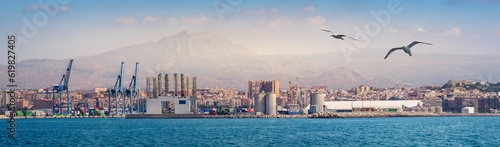 Industrial landscape of The Port of Alicante. Infrastructure of the seaport and cargo terminal with portal cranes and cargo containers storage. Global transportation hub on Mediterranean Sea in Spain.