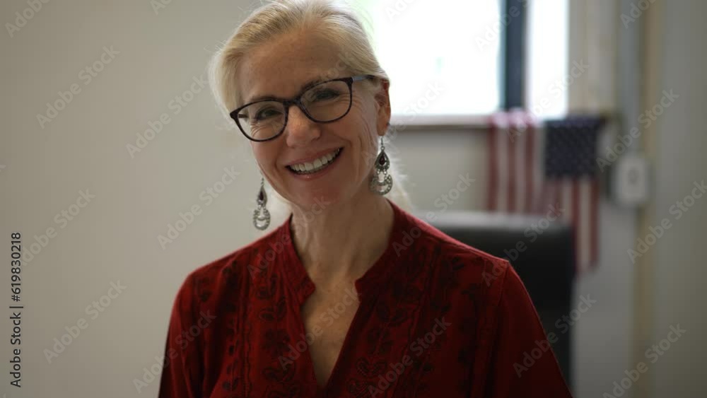 Portrait of happy smiling female teacher sitting on corner of her desk in a school classroom with US American flag behind her. Portrait of happy smiling female teacher sitting on corner of her desk in a school classroom with US American flag behind her.