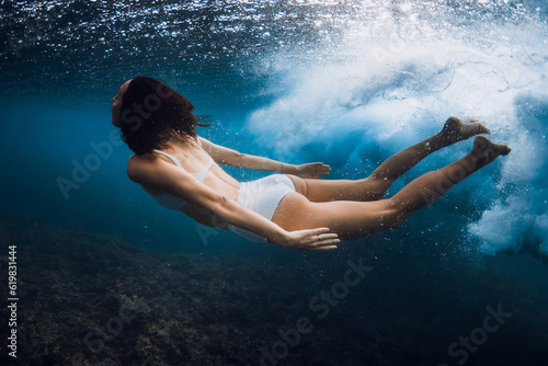 Woman without surfboard underwater with ocean wave. Duck dive under barrel wave