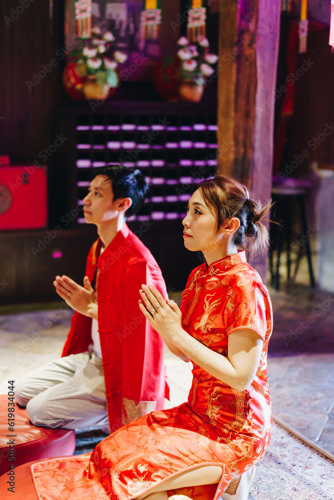 Obraz premium Happy young Asian couple in Chinese traditional dresses praying at temple