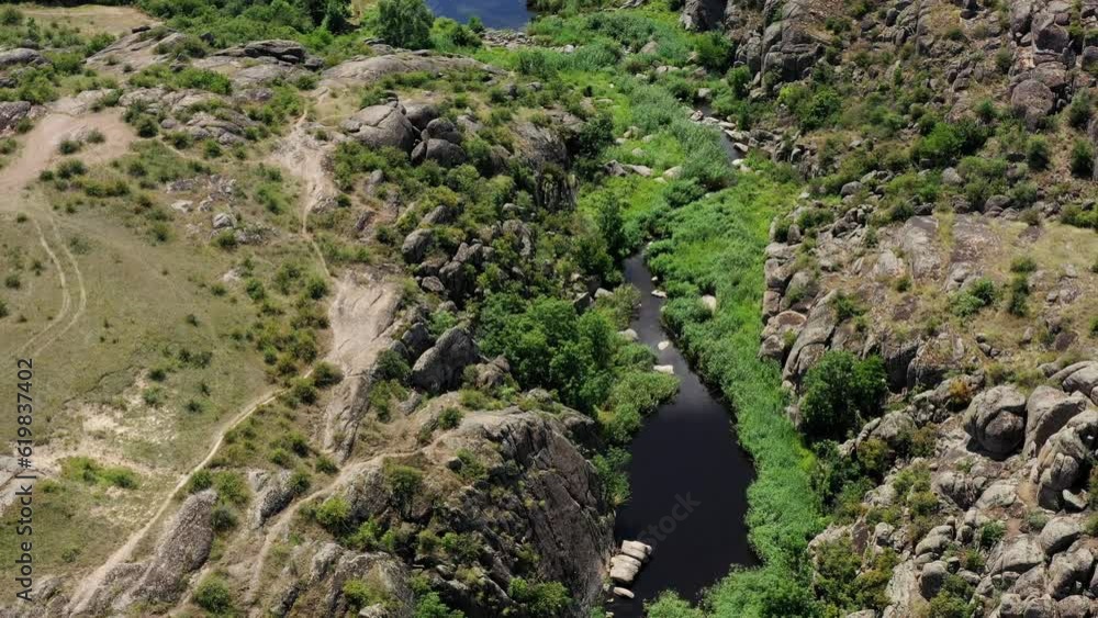 Bird's eye view of Aktovsky canyon of the Mertvovod river, Mykolaiv region, Ukraine. Shallow river flows at the bottom of the canyon in the environment greens and cliffs on summer sunny day. Bird's eye view of Aktovsky canyon of the Mertvovod river, Mykolaiv region, Ukraine. Shallow river flows at the bottom of the canyon in the environment greens and cliffs on summer sunny day.